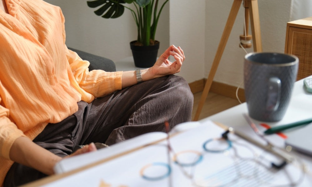 A person meditating with a cup of coffee next to them in an article about coffee and meditation.